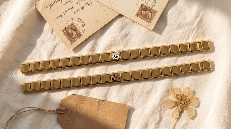 Goldene Italian Charm Armbänder mit Route-66- und Colosseum-Charm, umgeben von Postkarte, Gepäckanhänger und getrockneter Blume